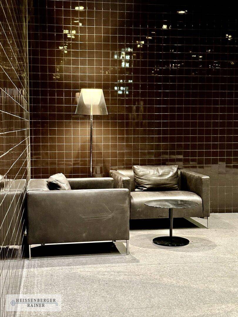 Detailansicht der Lobby mit bequemen Ledersesseln, Stehlampe und dunklen Fliesenwänden.