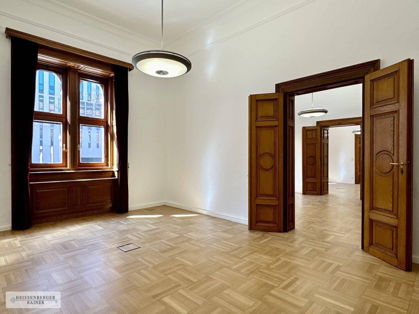Geräumiges, leeres Büro mit klassischem Fischgrätparkett, hohen Decken und großen Fenstern, bereit zur Einrichtung.
