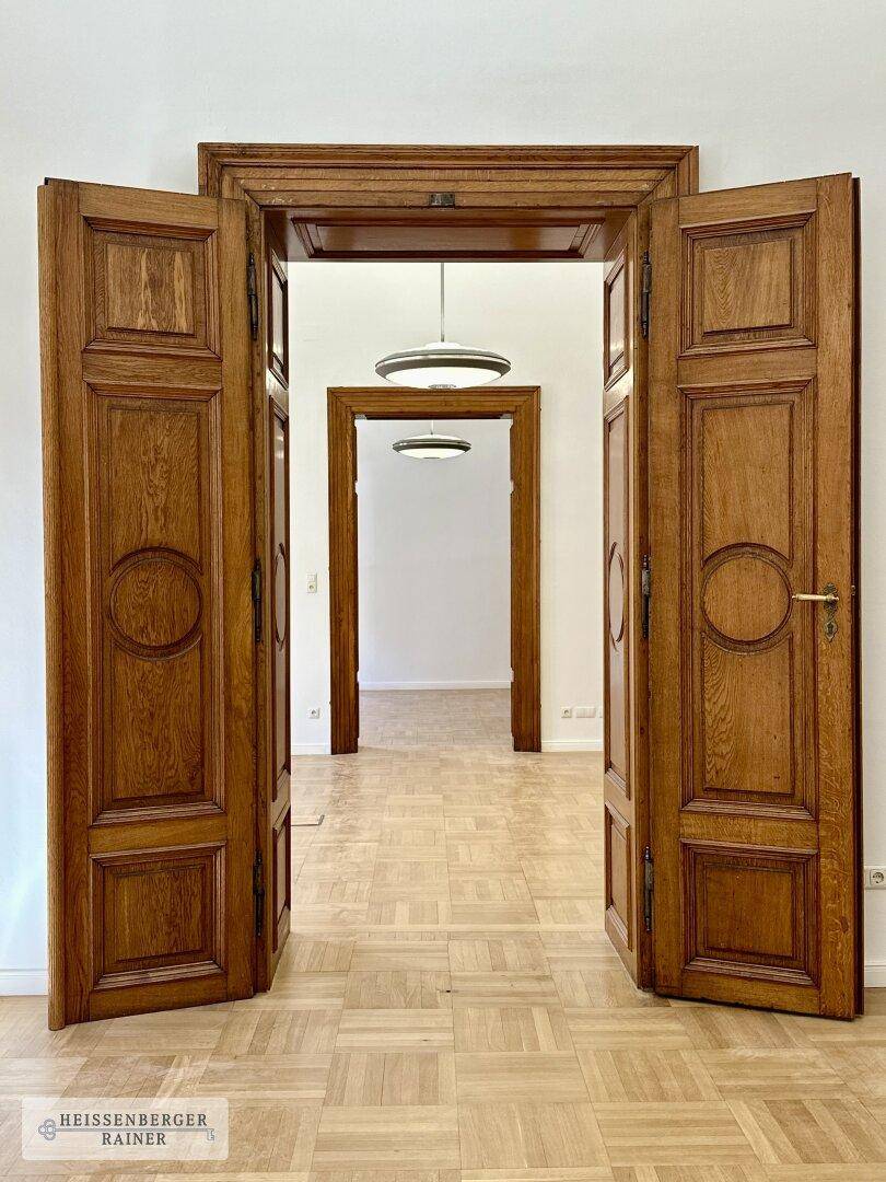 Symmetrische Ansicht durch mehrere offene Holztüren, die eine elegante Raumflucht mit Parkettboden zeigen.