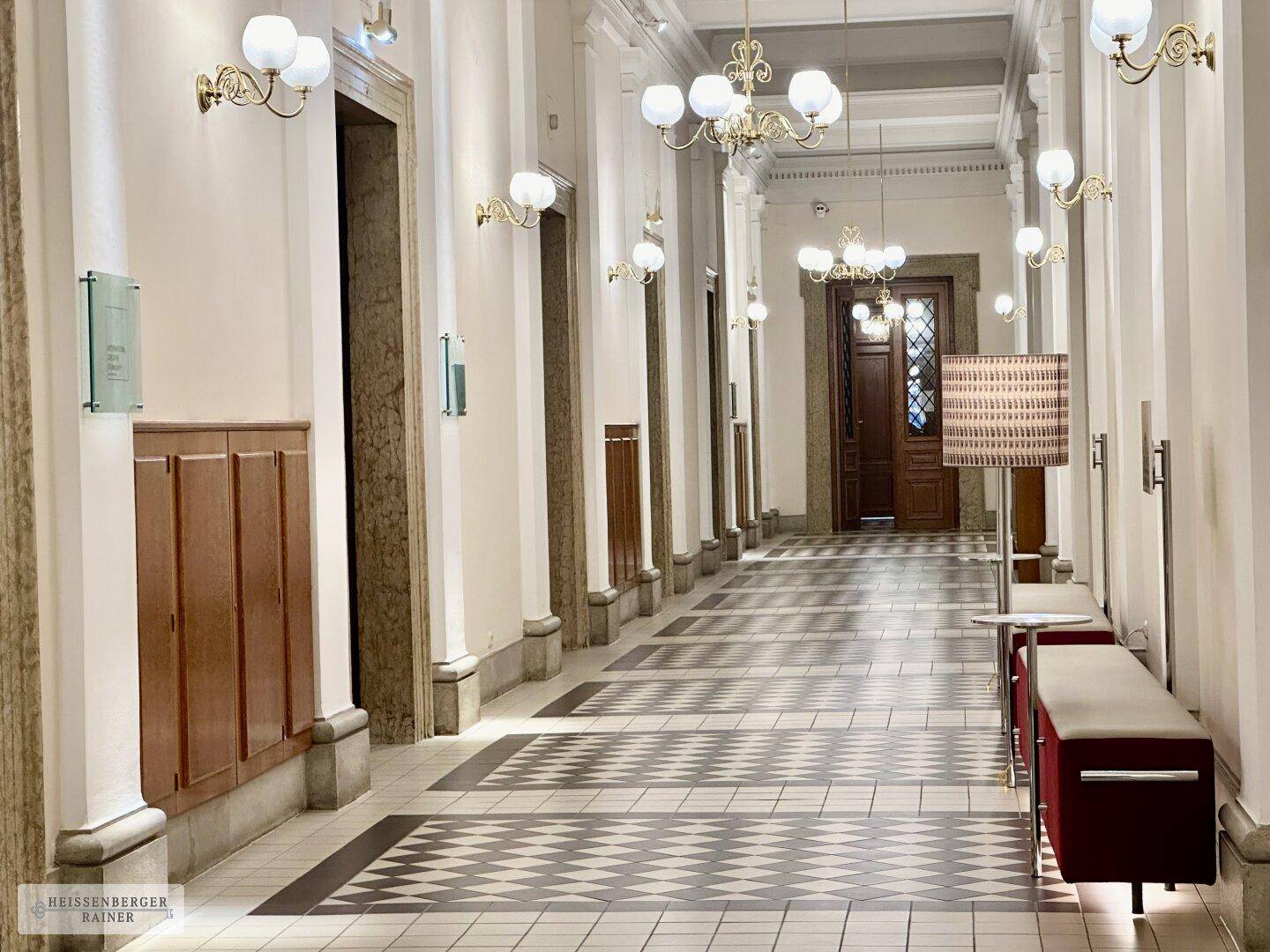 Prunkvoller Flur mit gemusterten Fliesen, hohen Decken und opulenten Wandleuchten und Kronleuchtern.