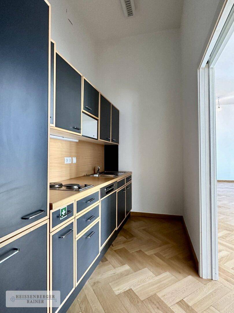 Funktionale Teeküche mit dunklen Schränken, Holztheke und Fischgrätparkett in einem Bürobereich.