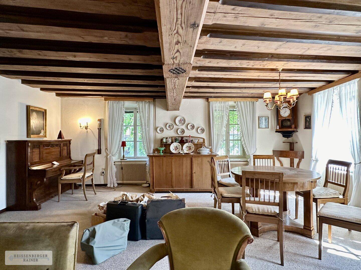 Geräumiges Wohnzimmer mit freiliegenden Holzbalken, traditionellen Möbeln und einem Klavier.