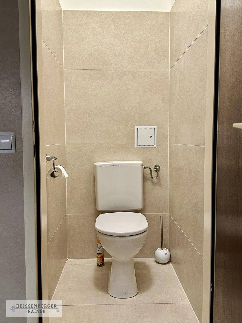 Separate Toilette mit beigefarbenen Fliesen und wandmontiertem WC.