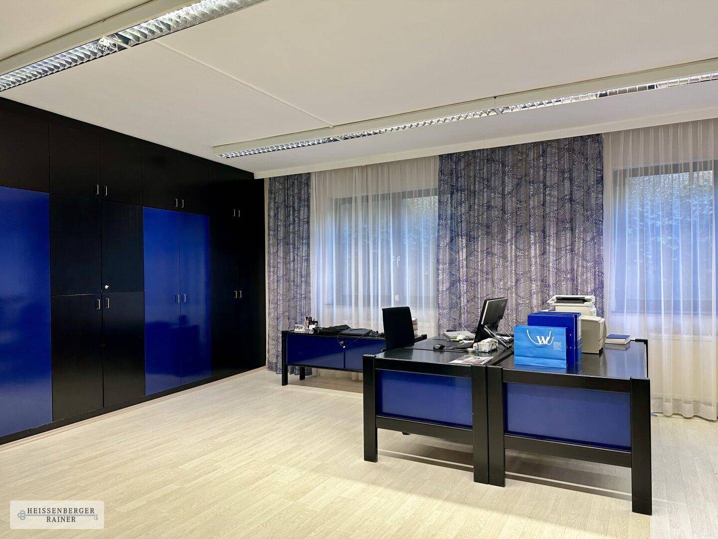 Modernes Büro mit blauen und schwarzen Schränken, hellen Böden und großen Fenstern.