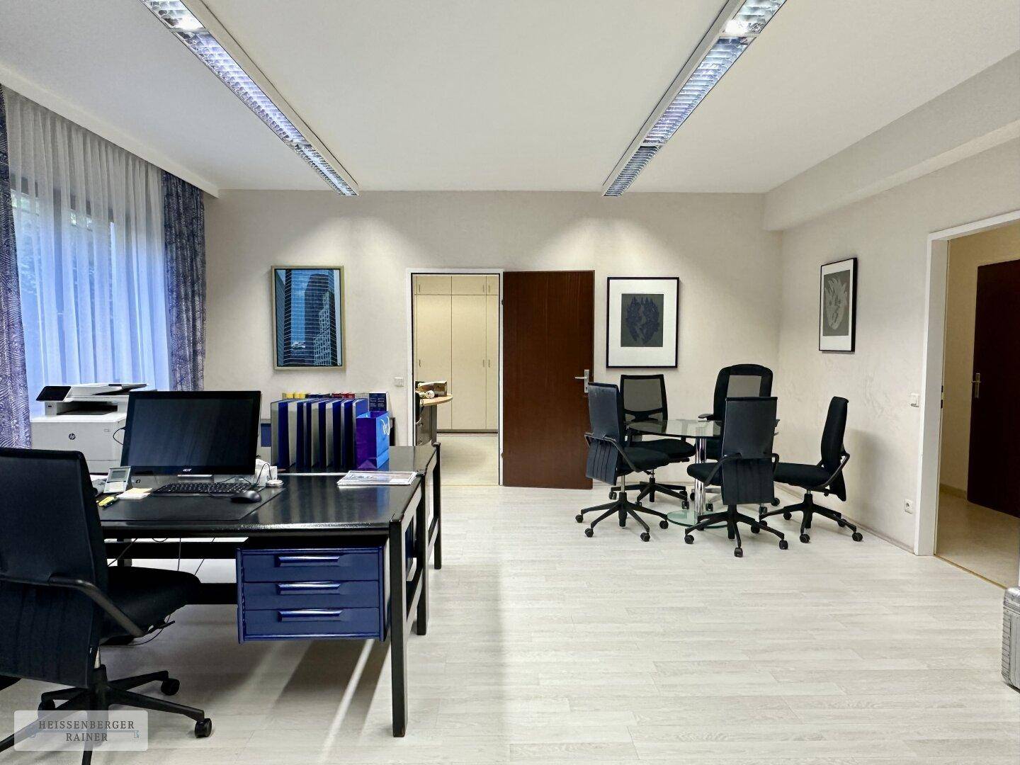 Helles Büro mit mehreren Arbeitsbereichen, Besprechungstisch und Blick auf den Flur.