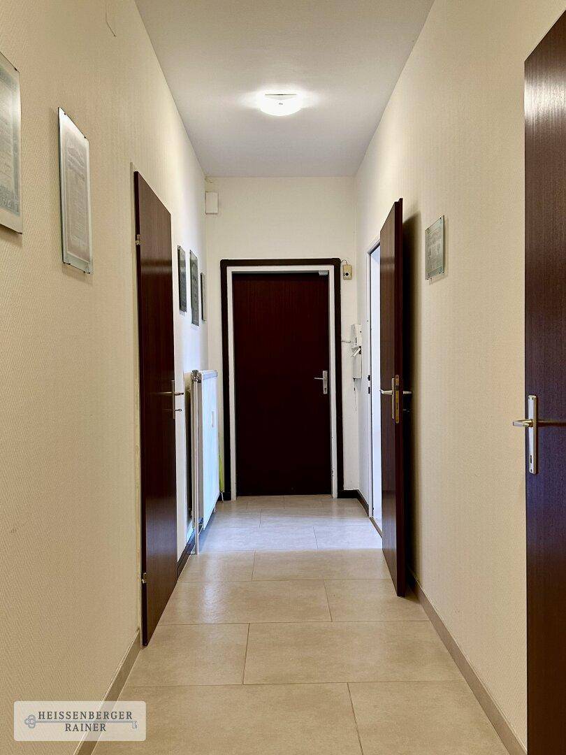 Langer Flur mit mehreren Türen, hellem Fliesenboden und Deckenbeleuchtung.