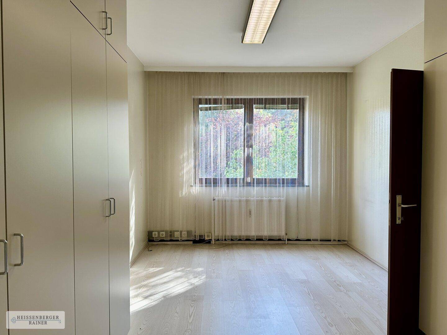 Leeres Büro mit Einbauschränken, Fenster und hellem Laminatboden.
