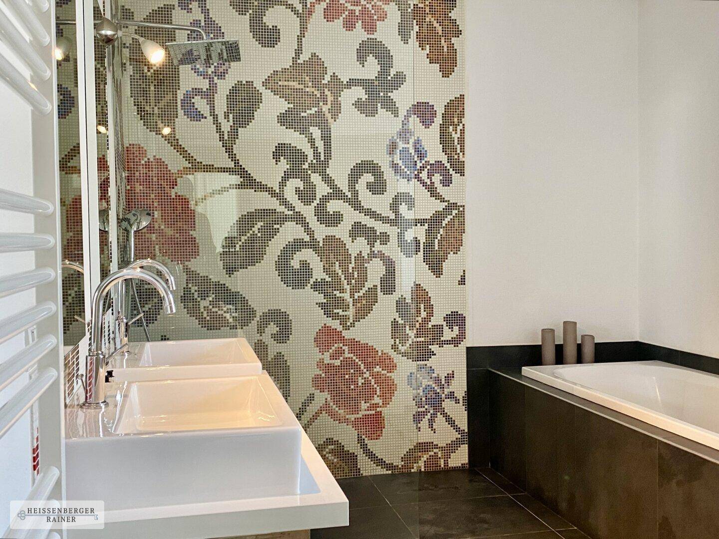 Modernes Badezimmer mit Doppelwaschbecken, Badewanne und dekorativer Mosaikwand.