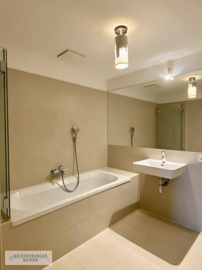 Modernes Badezimmer mit Badewanne, Dusche, Einzelwaschbecken und großem Spiegel, in beigen Farbtönen.