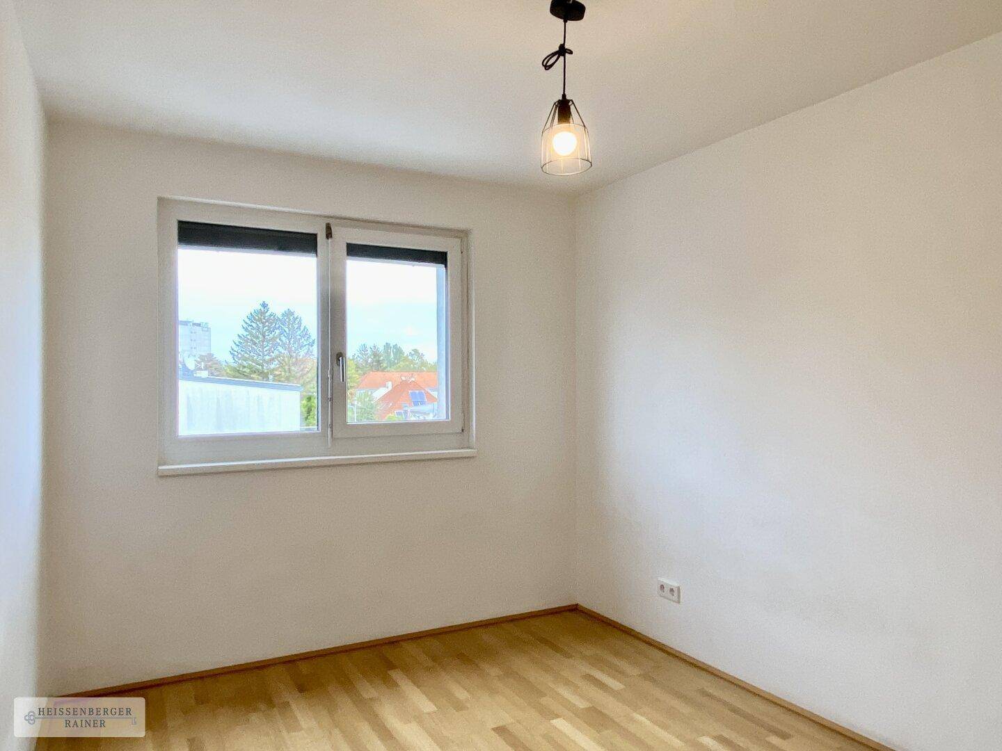 Leeres Zimmer mit Holzboden und Fenster, bietet viel Tageslicht und flexible Nutzungsmöglichkeiten.
