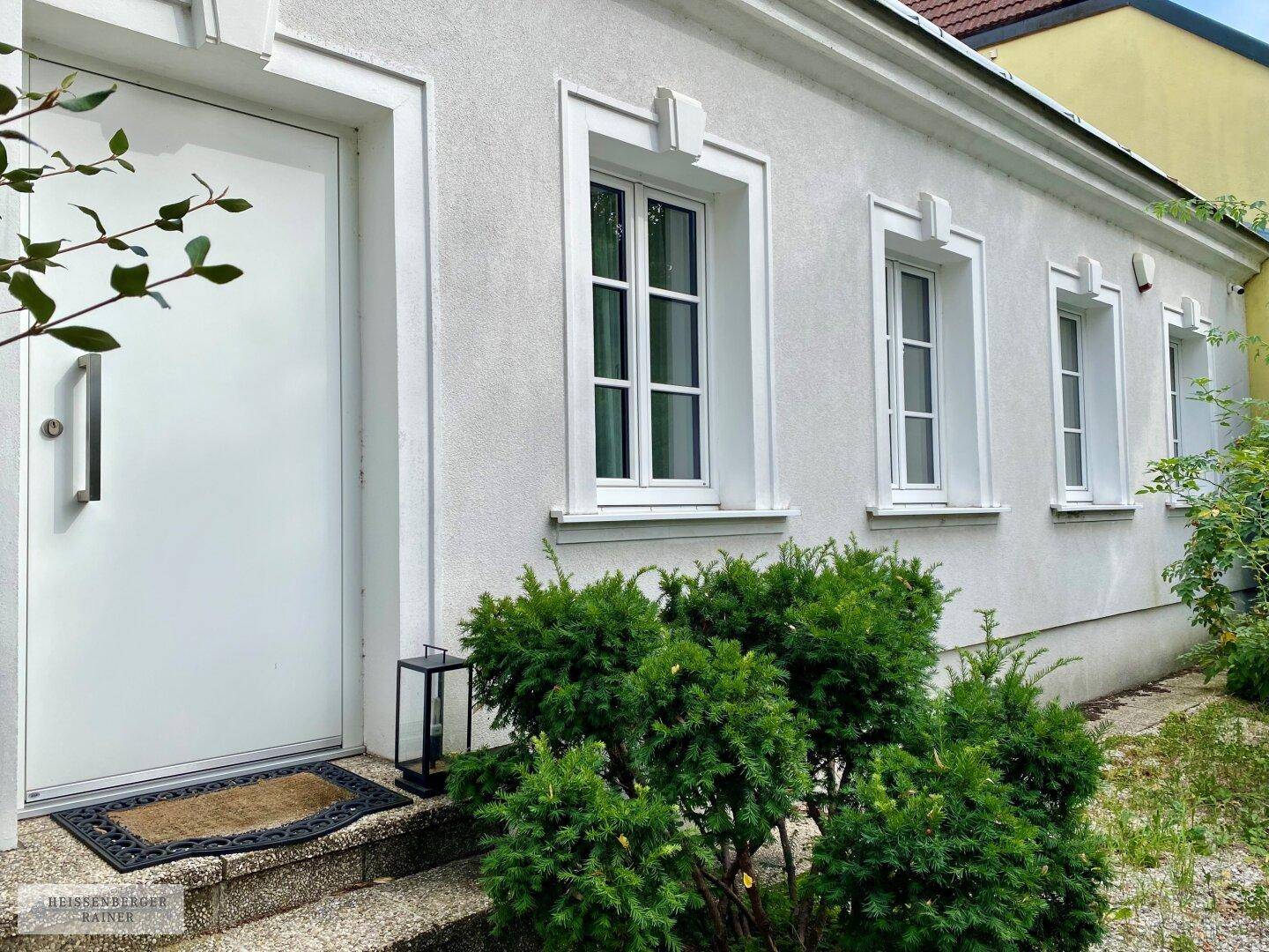Attraktive Hausfassade mit weißem Putz, modernen Fenstern und gepflegten Büschen am Eingangsbereich.