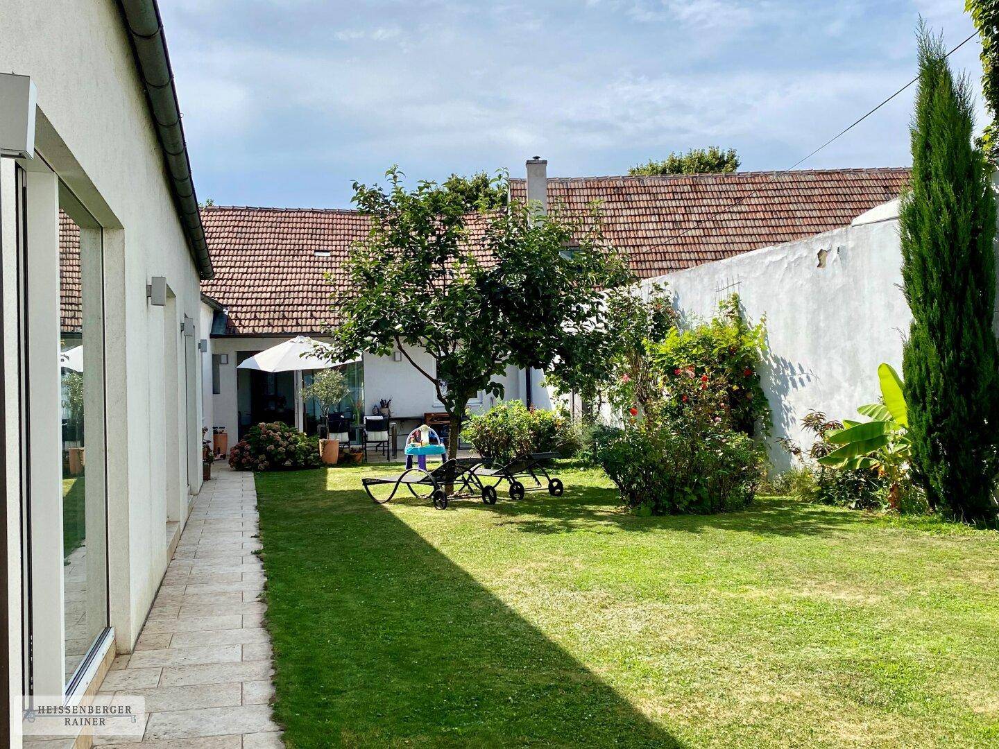 Gepflegter Garten mit Rasenfläche, Bäumen und einem sonnigen Bereich zum Entspannen im Freien.