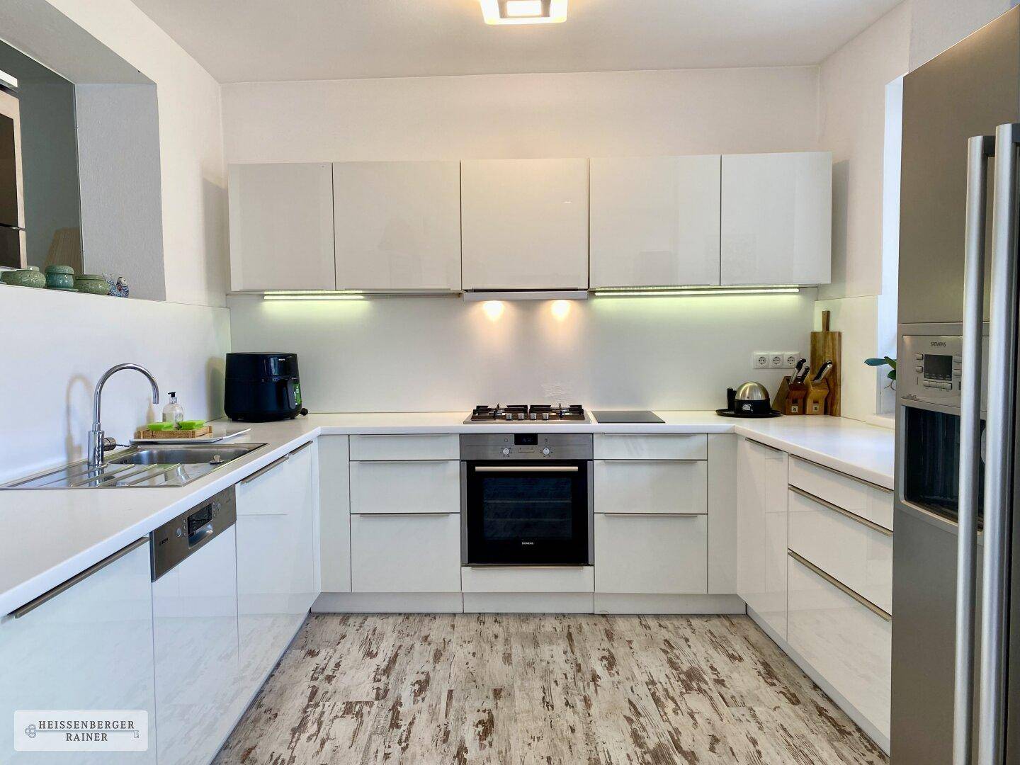 Moderne Küche mit weißen Hochglanzfronten, integrierten Geräten und hellem Holzboden.