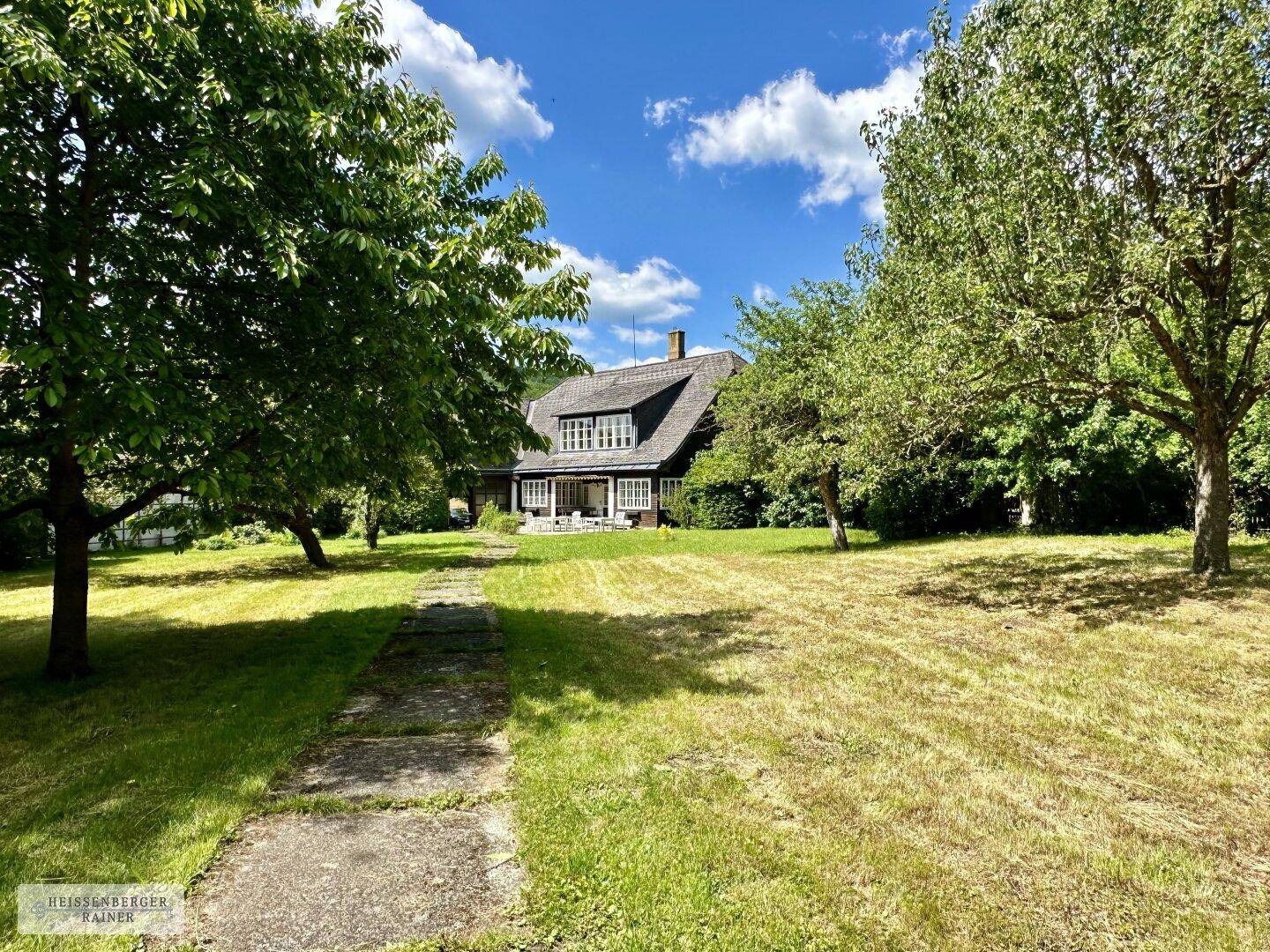 Weitläufiger Garten mit altem Baumbestand und einem charmanten Landhaus im Hintergrund.