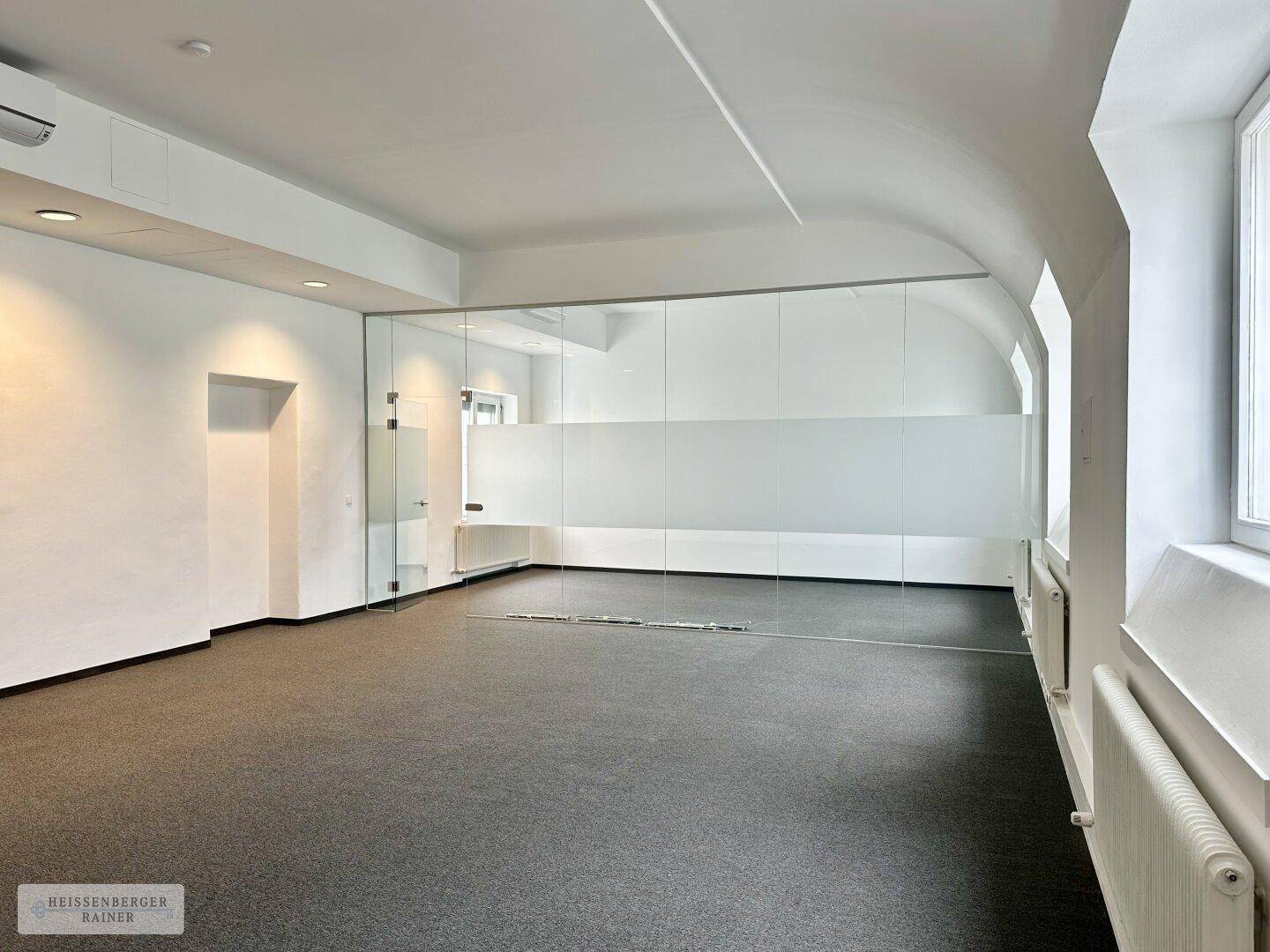 Helles Büro mit Teppichboden, weißen Wänden und einer eleganten Glaswand, die den Raum strukturiert.