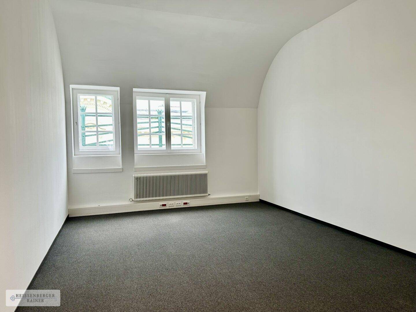 Kleineres Büro mit Teppichboden, weißen Wänden und zwei charmanten Bogenfenstern, die Tageslicht hereinlassen.
