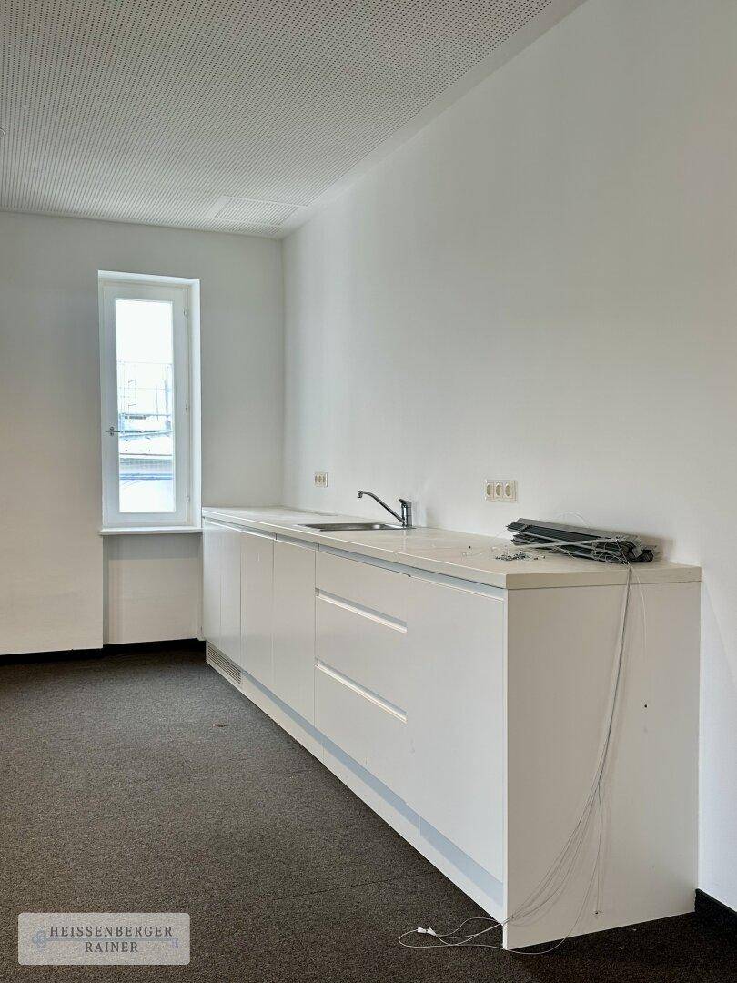 Kleine, funktionale Küchenzeile mit weißen Schränken, Spüle und einem Fenster für natürliches Licht.