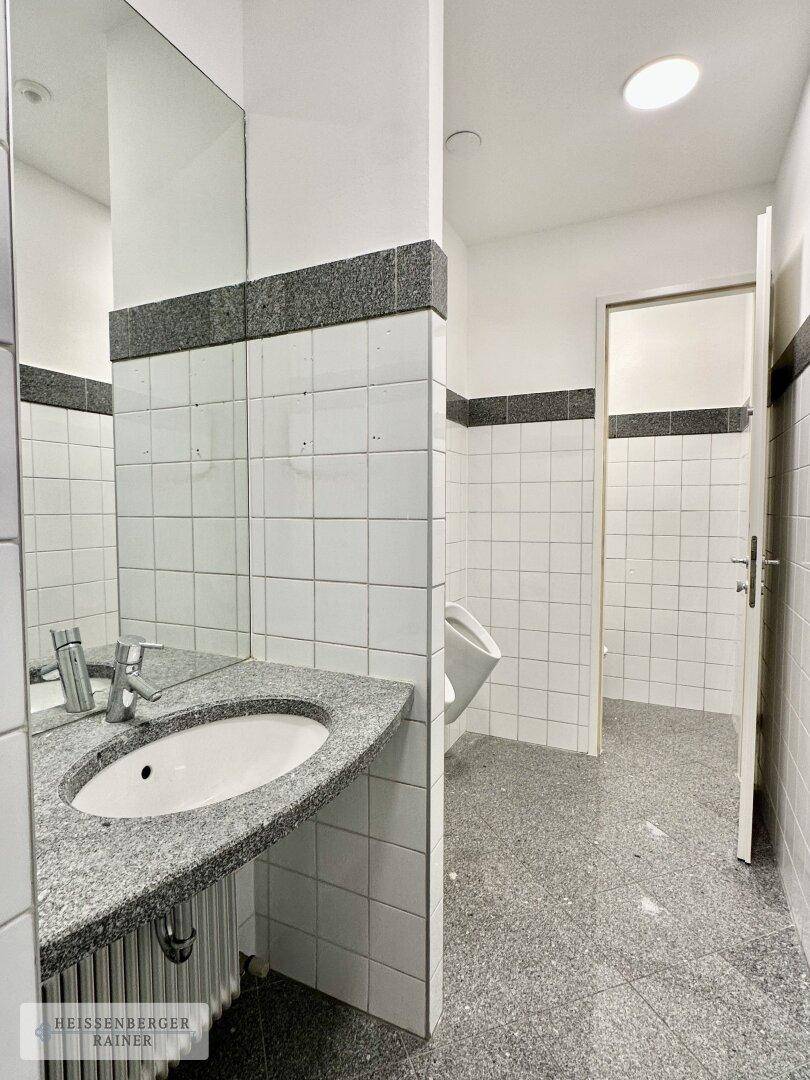 Gefliester Waschraum mit Granitwaschtisch, Spiegel und einem Urinal, in einem funktionalen Design.