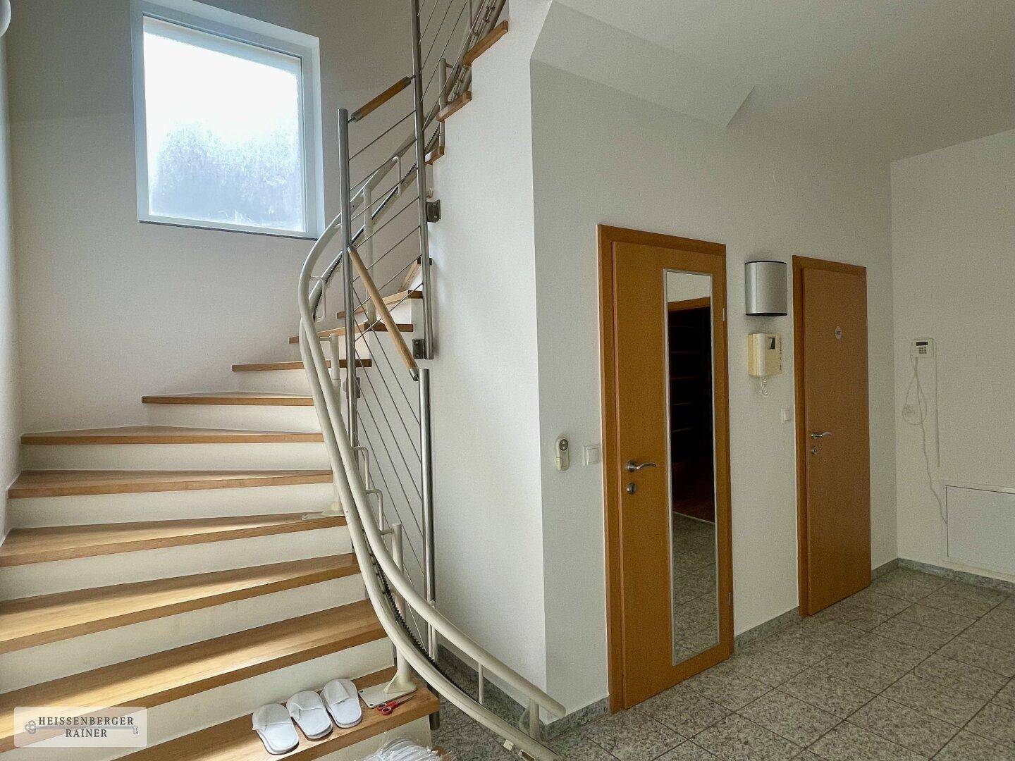 Heller Flur mit eleganter Holzwendeltreppe und Fliesenboden.