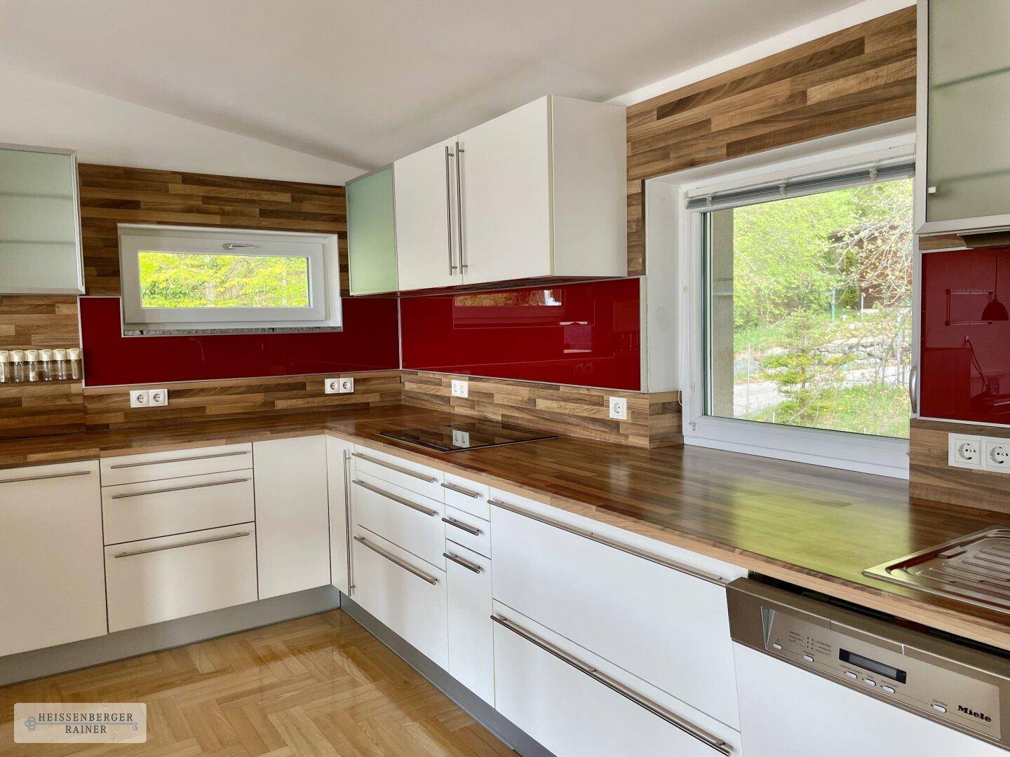 Helle Küche mit weißen Fronten, Holzarbeitsplatten, roter Rückwand und Induktionskochfeld.