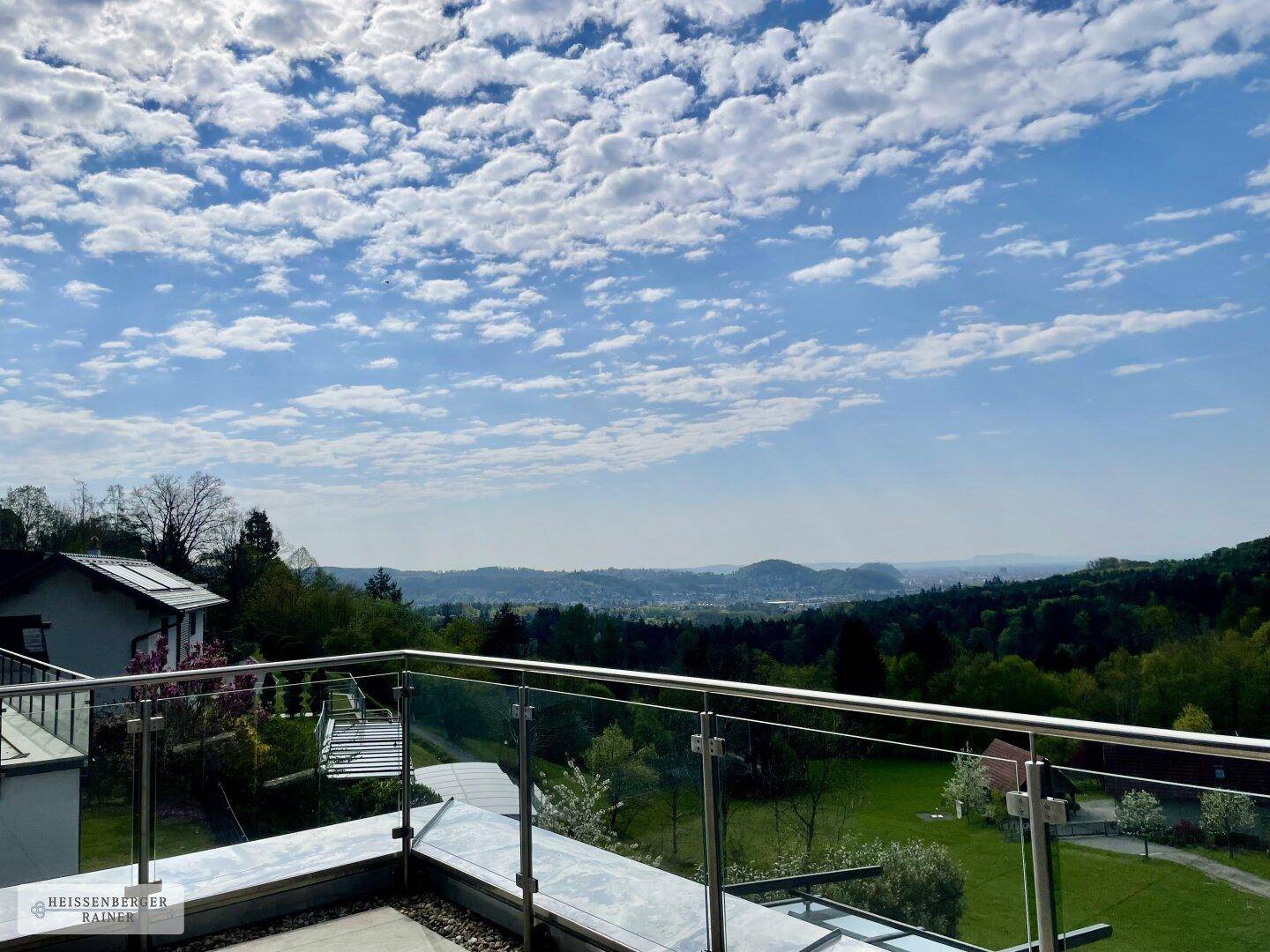 Weitläufiger Ausblick von der Terrasse über eine grüne Hügellandschaft unter blauem Himmel.