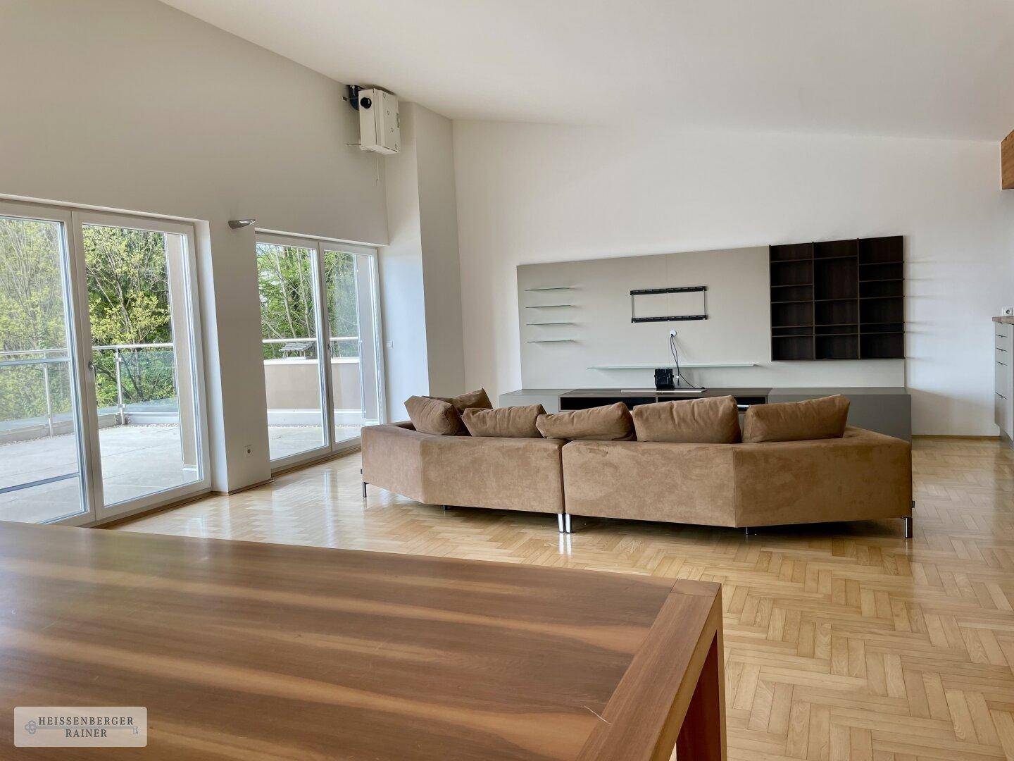 Heller Wohnbereich mit großem Sofa, Fischgrätparkett und Zugang zu einer weitläufigen Terrasse.