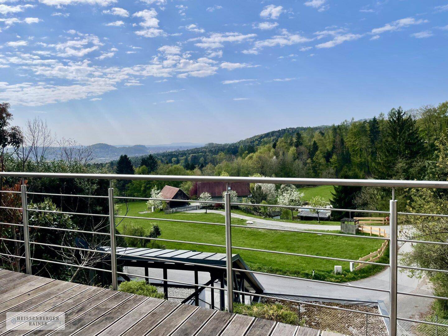 Großer Holzbalkon mit Edelstahlgeländer und weitem Blick ins grüne Umland und die Natur.