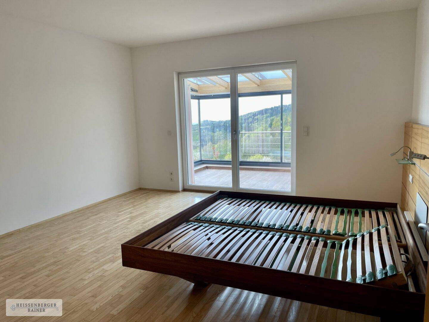 Schlafzimmer mit Holzboden und großen Schiebetüren, die zu einem verglasten Wintergarten führen.