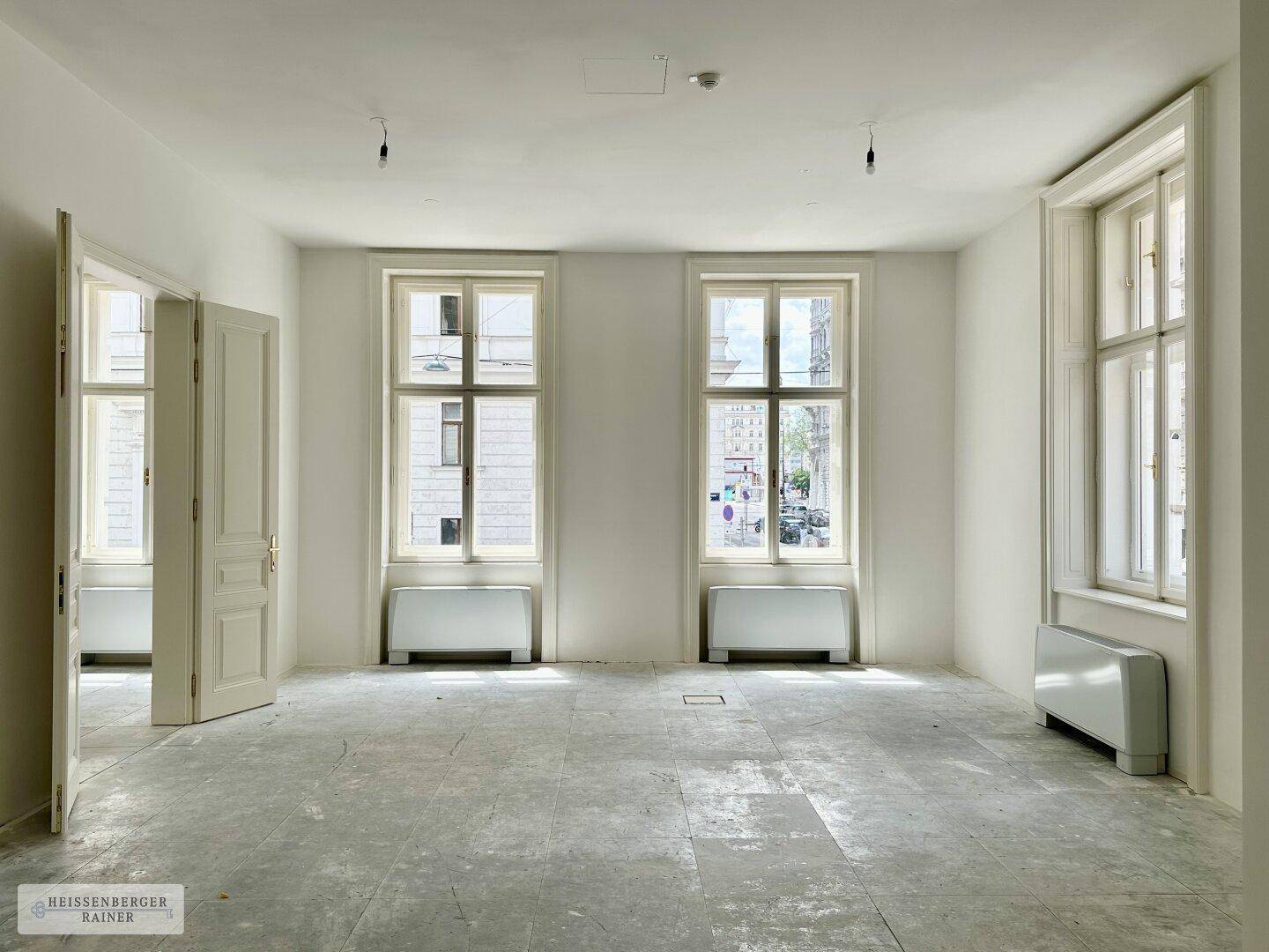 Heller Raum mit hohen Fenstern, die einen Blick auf die Stadtstraße ermöglichen, und Heizkörpern.