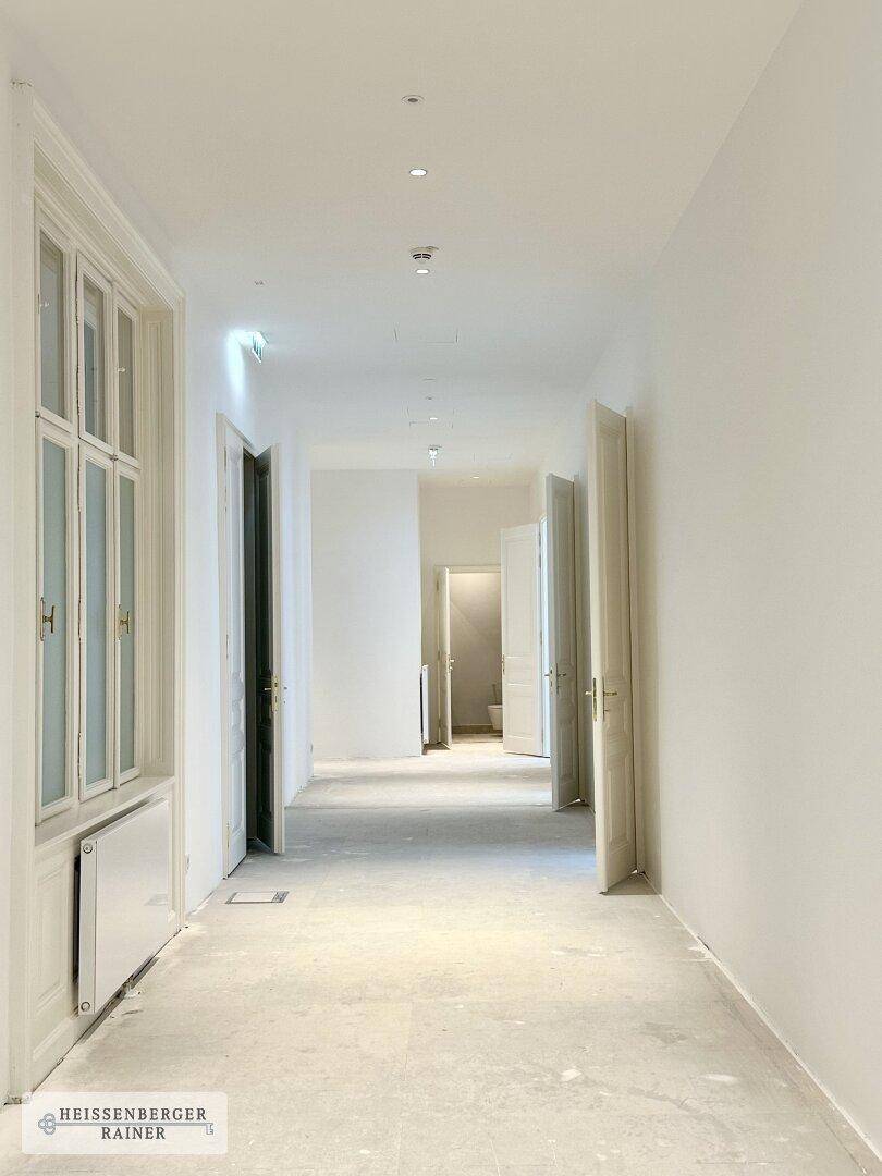 Langer, heller Flur mit mehreren Türen und Fenstern, die Tageslicht hereinlassen.