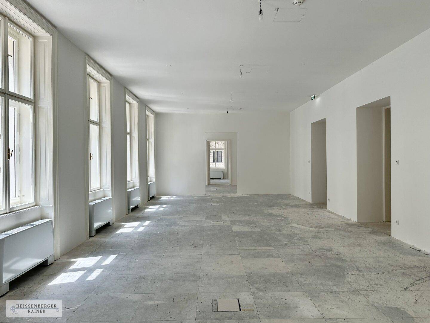 Geräumiger, heller Innenraum mit einer Reihe hoher Fenster und vorbereitetem Bodenbelag.