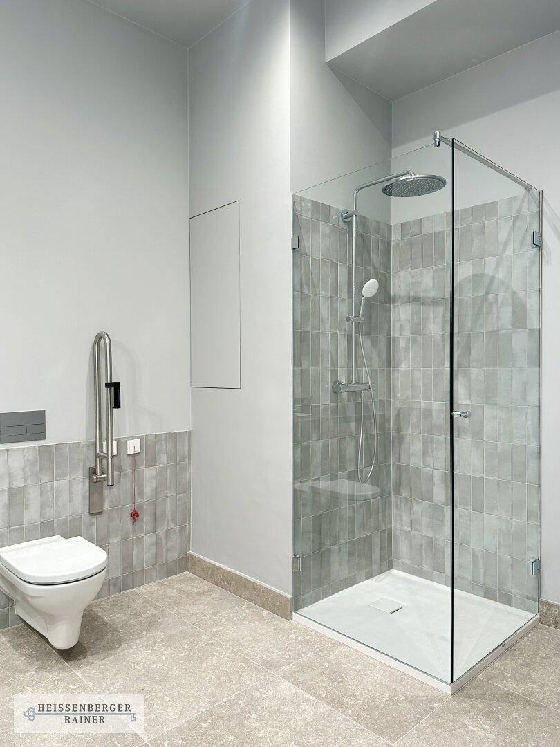 Modernes Badezimmer mit ebenerdiger Dusche, WC und grauen Wand- und Bodenfliesen.