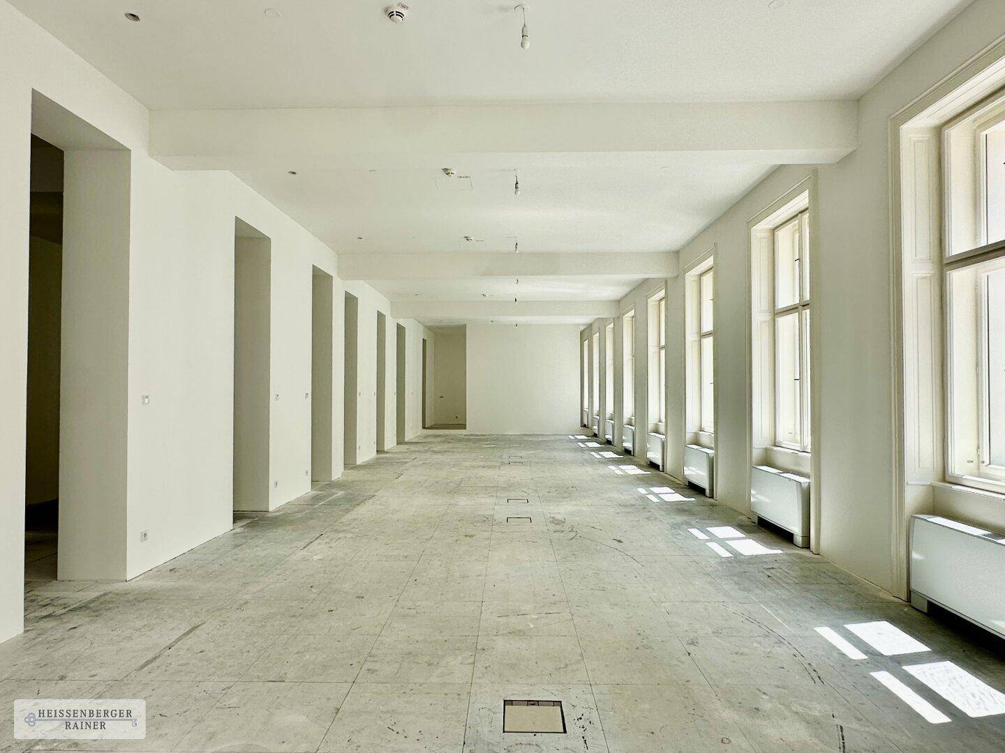 Weitläufiger, lichtdurchfluteter Bürobereich mit hohen Decken und vielen Fenstern, ideal für Großraumbüros.