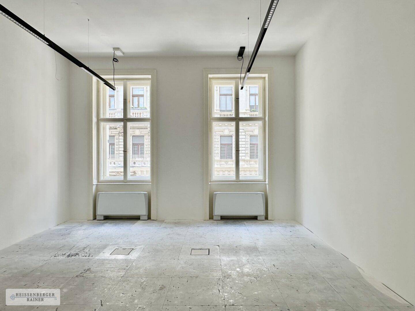 Heller Büroraum mit zwei großen Fenstern und moderner Deckenbeleuchtung, bereit zur Einrichtung.