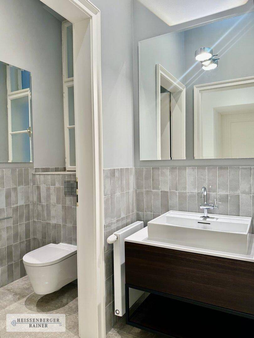 Modernes Badezimmer mit grauen Fliesen, wandhängendem WC und stilvollem Waschtisch.