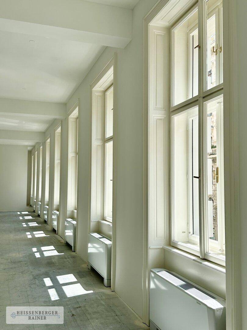 Eine Reihe hoher Fenster mit Heizkörpern darunter, die viel natürliches Licht in den Raum bringen.
