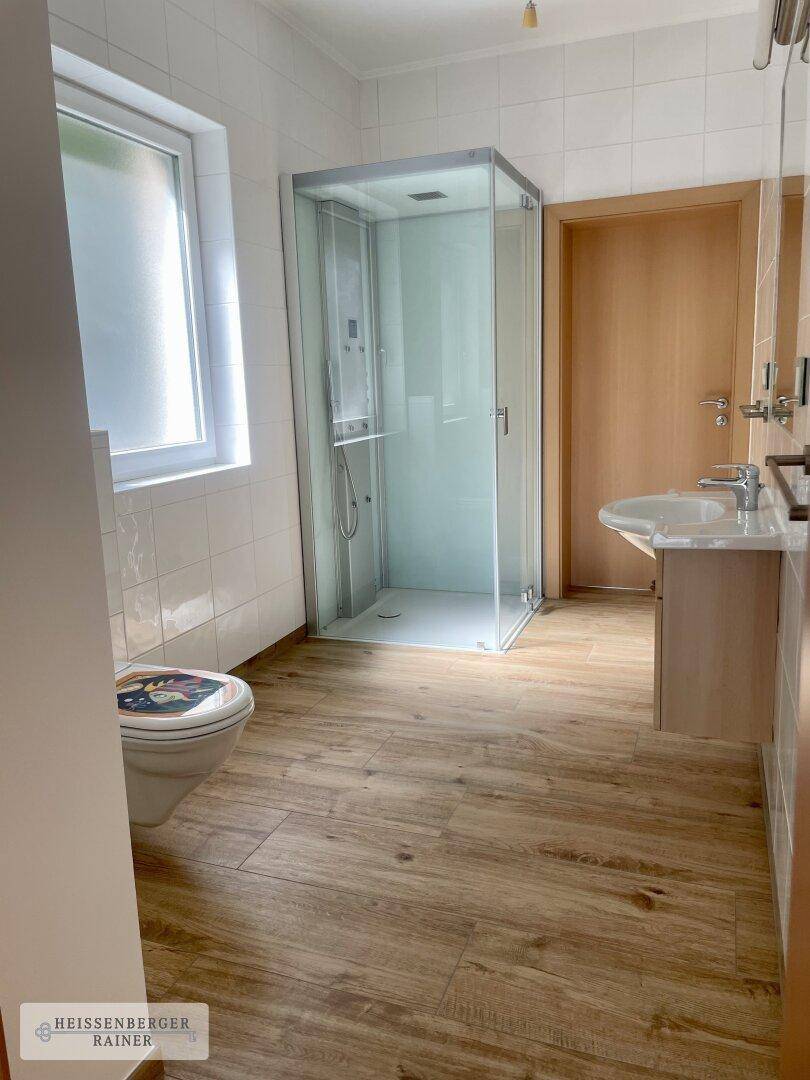 Badezimmer mit Duschkabine, WC und Waschbecken, ausgestattet mit Holzoptik-Fliesen.