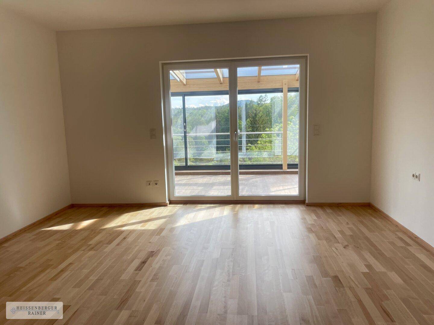 Helles Zimmer mit Holzboden und großen Schiebetüren, die zu einem verglasten Außenbereich führen.