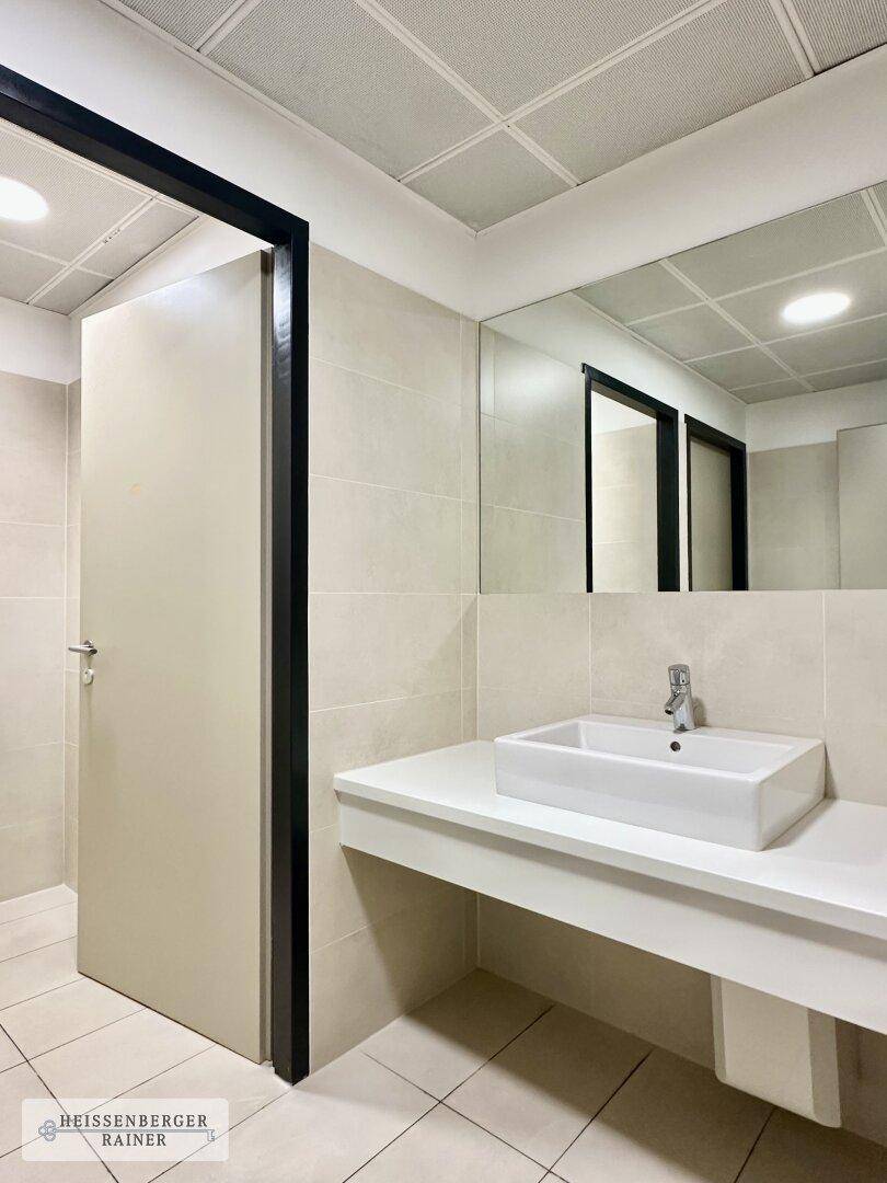 Modernes Badezimmer mit Aufsatzwaschbecken, großem Spiegel und hellen Fliesen an Boden und Wänden.