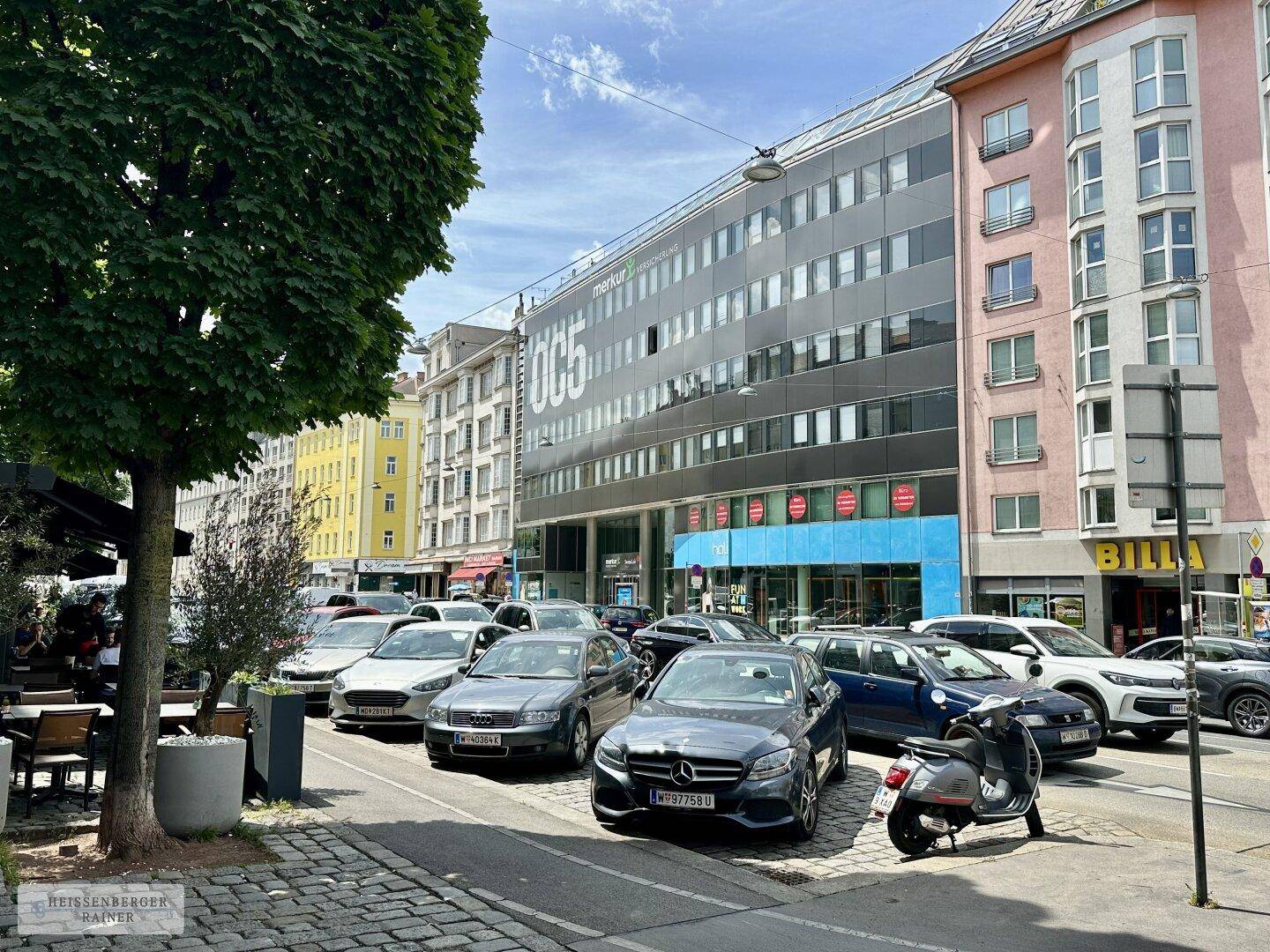 Straßenansicht eines modernen Bürogebäudes mit Geschäften und parkenden Autos.