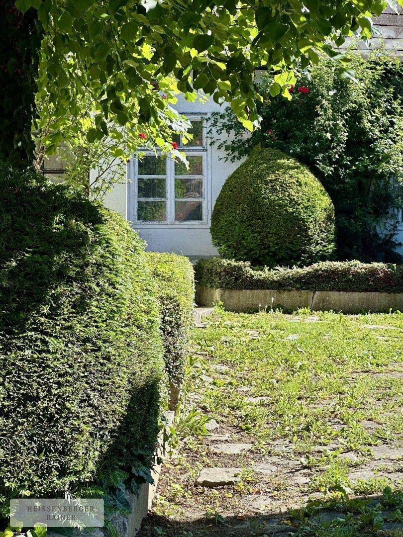 Gartenweg führt durch gepflegte Hecken und Sträucher zu einem Fenster des Hauses.