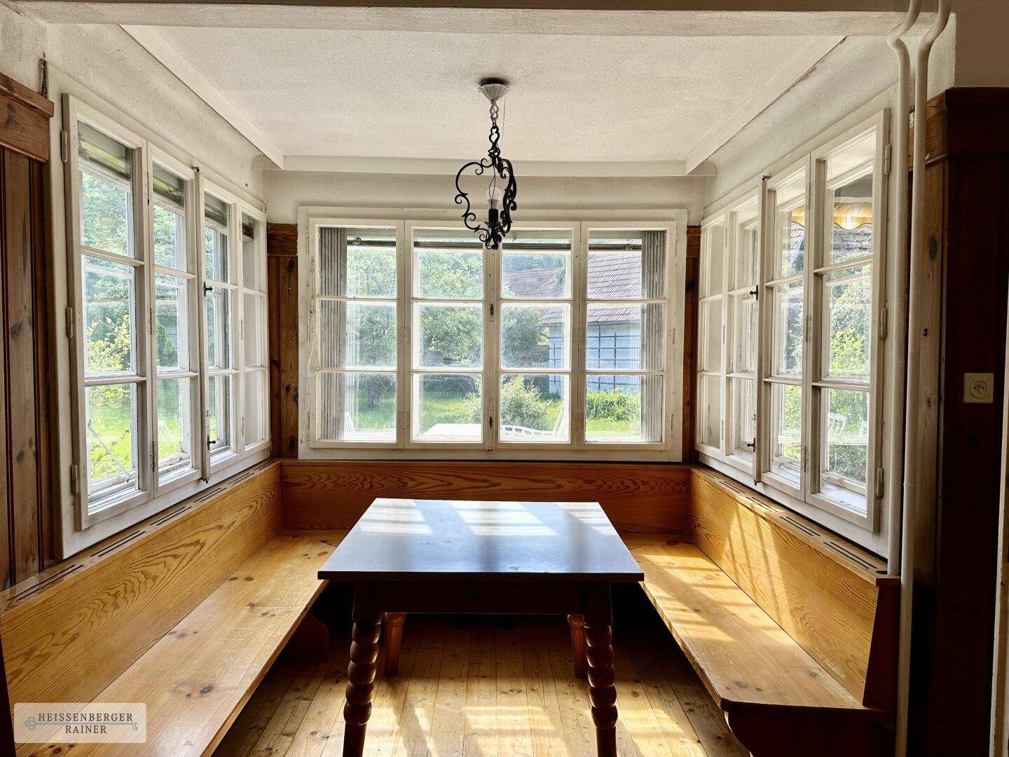 Heller Essbereich mit vielen Fenstern, Holzbänken und einem rustikalen Holztisch.