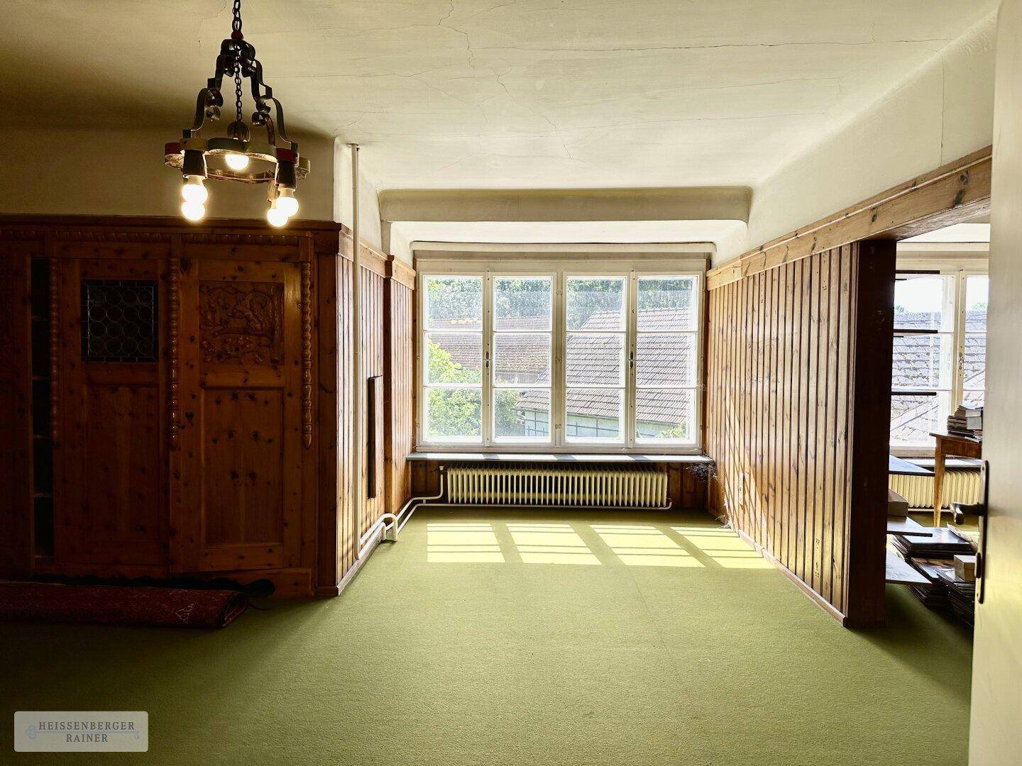 Geräumiger Raum mit Holzvertäfelung, grünem Teppichboden und einem großen Fenster.
