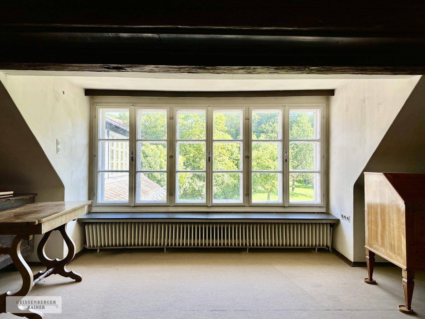 Heller Raum im Dachgeschoss mit großen Fenstern und Blick ins Grüne, unmöbliert.