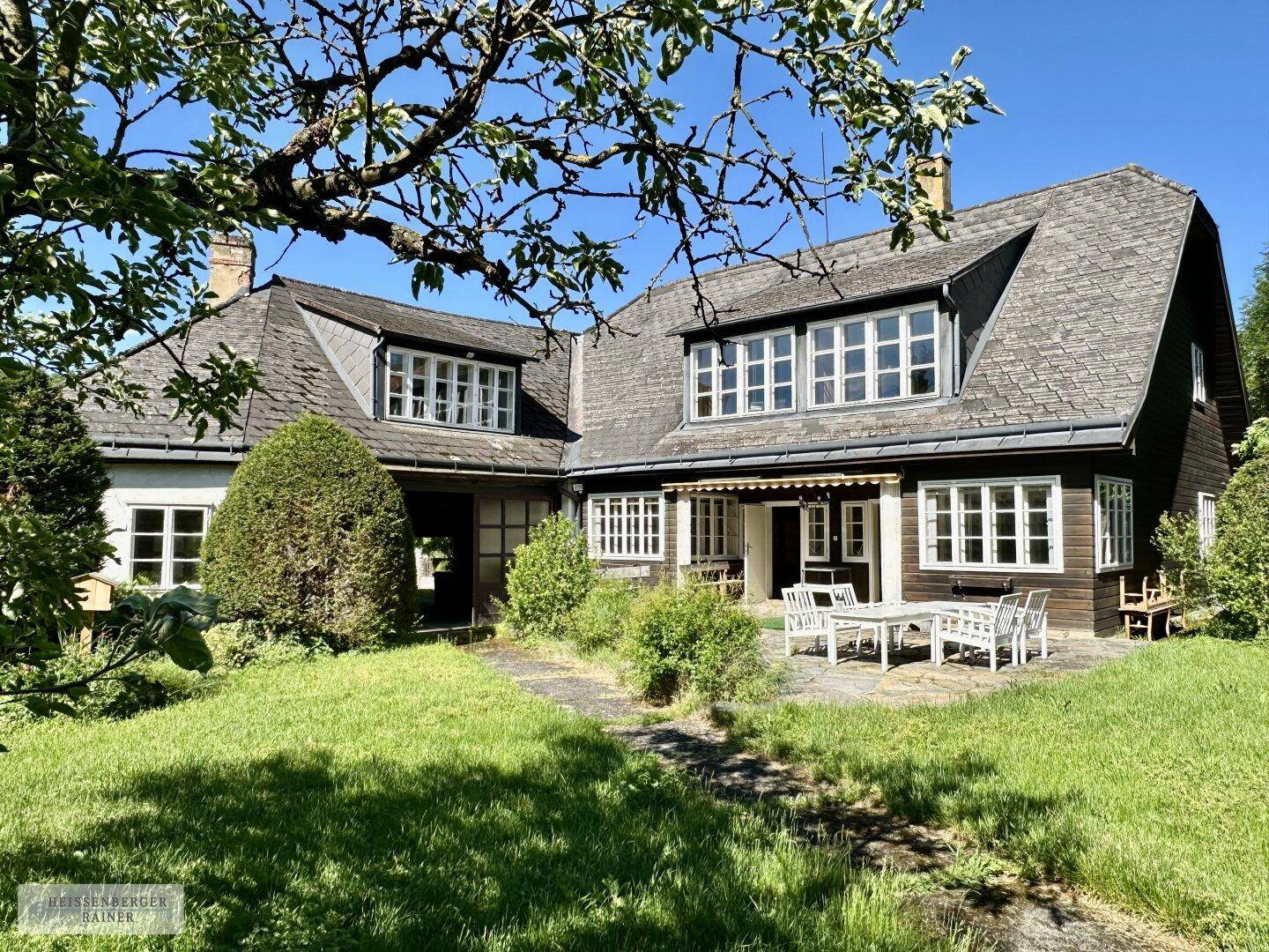 Charmantes Landhaus mit Mansarddach, umgeben von einem gepflegten Garten und einer sonnigen Terrasse.