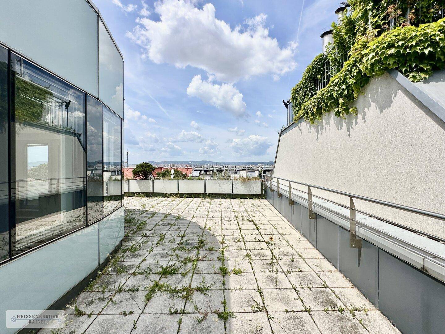 Lange, gepflasterte Terrasse mit Begrünung und Blick auf die umliegende Stadtlandschaft.