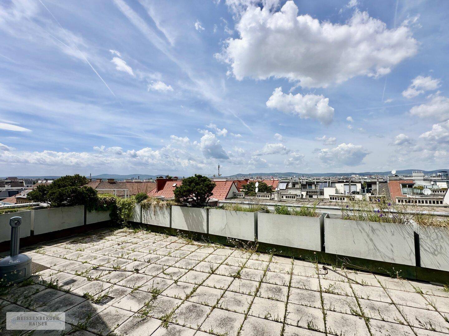 Weitläufige Dachterrasse mit Pflanzkübeln und Panoramablick über die Dächer der Stadt.