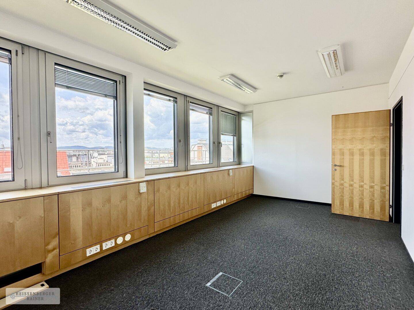 Funktionaler Büroraum mit Teppichboden, Holzverkleidung und großen Fenstern.