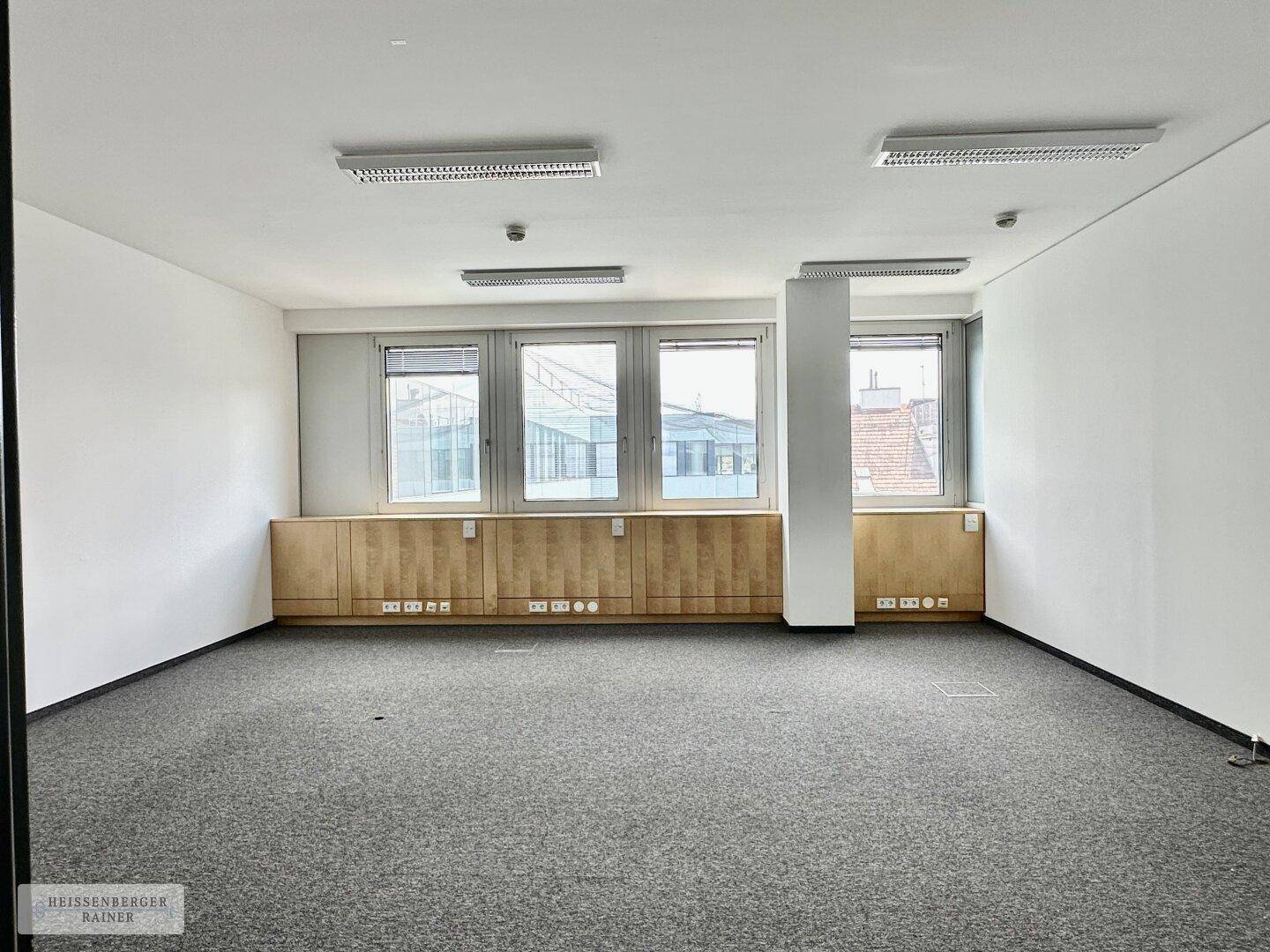 Geräumiger Büroraum mit Teppichboden, Säule und Fenstern mit Blick auf die Umgebung.