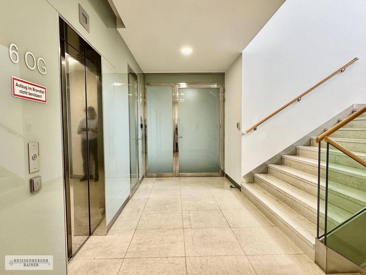 Heller Flur mit Aufzug, Treppe und Steinboden in einem modernen Gebäude.